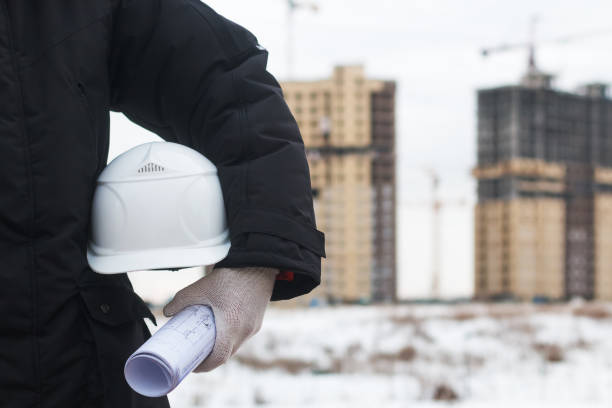 istock Architect or engineer holding yellow helmet for workers security on background of new highrise apartment buildings and construction cranes on background of winter landscape Silhouette Crane lifts load 855438994