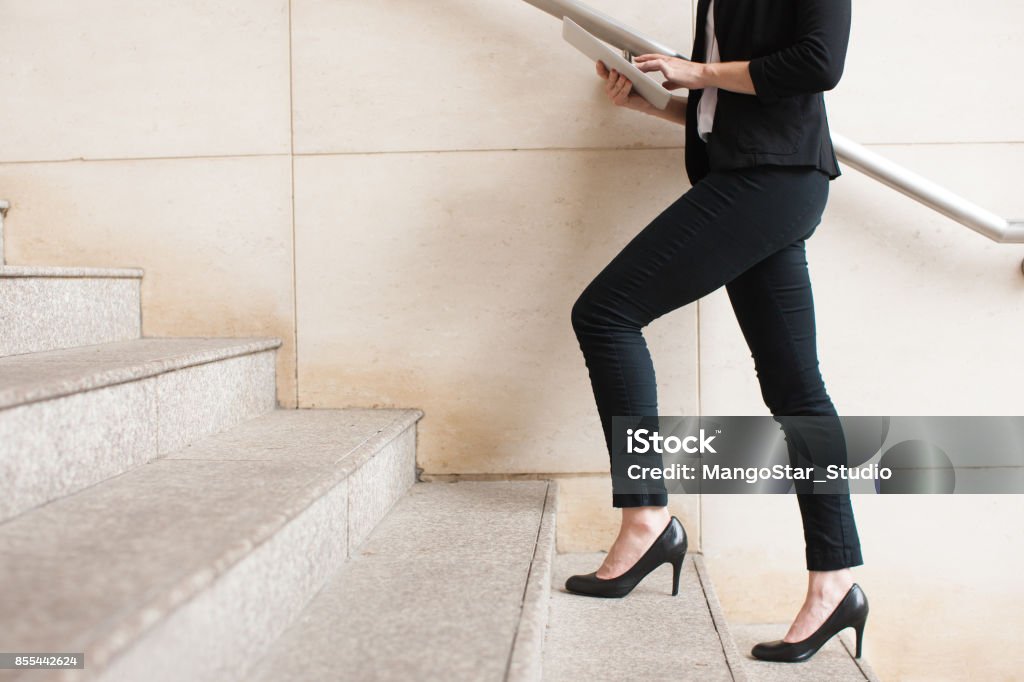 Businesswoman walking upstairs and using touchpad Portrait of young Caucasian businesswoman wearing high-heeled shoes walking upstairs and using digital tablet. Business concept High Heels Stock Photo