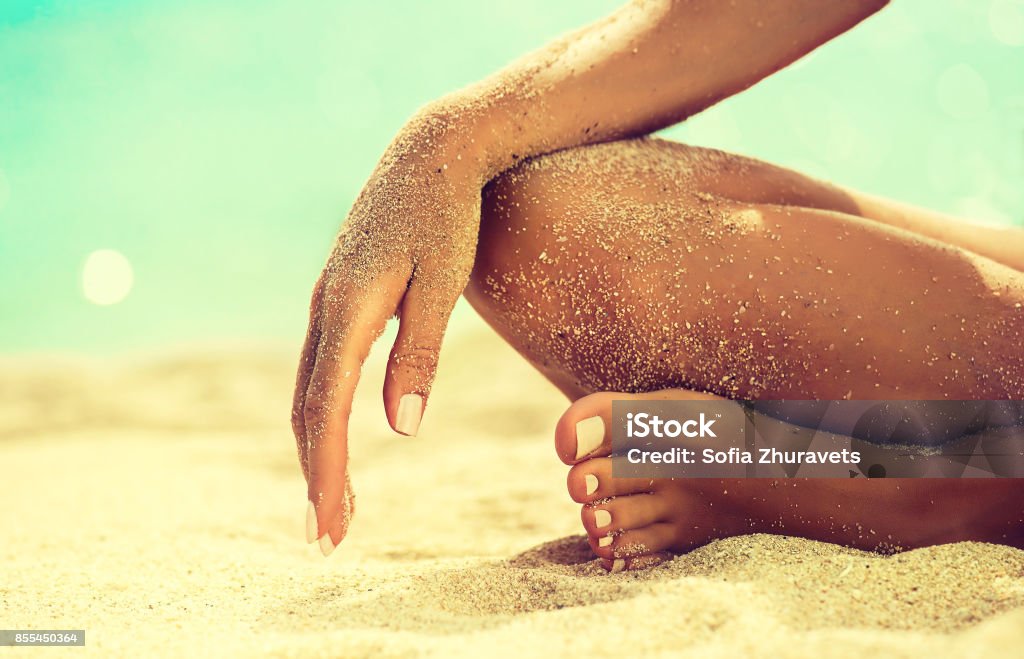 Womans hand is laying on the covered by sea sand knee. Body parts, Womans hand is laying on the covered by sea sand knee. Symbol of rest and relaxation on tropical beach. Tanned girl in Lotus position yoga and meditation. Foot Stock Photo