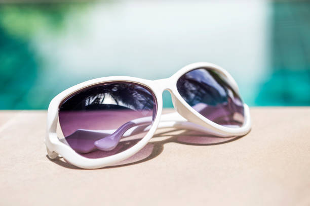 Design white sunglasses on swimming pool edge over blurred blue water background, outdoor day light