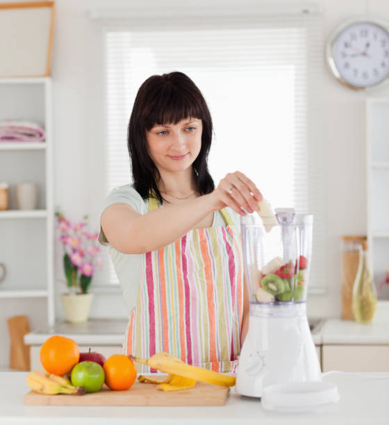 istock Attractive brunette woman putting vegetables in a mixer while standing 855466794
