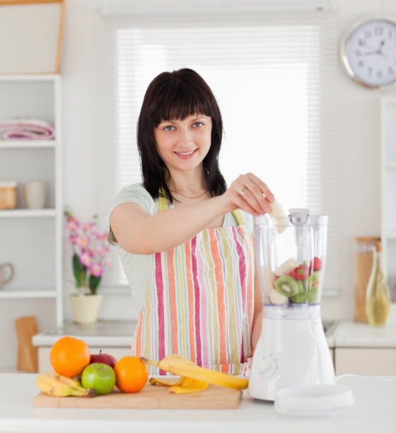 istock Beautiful brunette woman putting vegetables in a mixer while standing 855466844