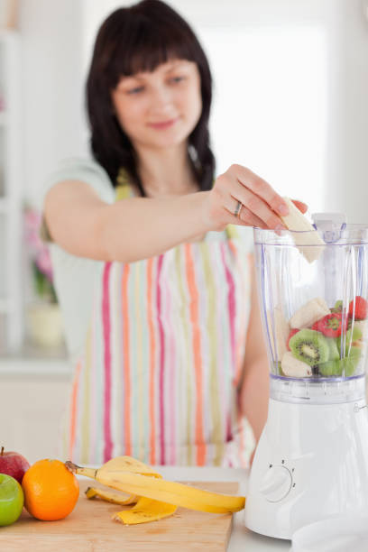 istock Charming brunette woman putting vegetables in a mixer while standing 855466912