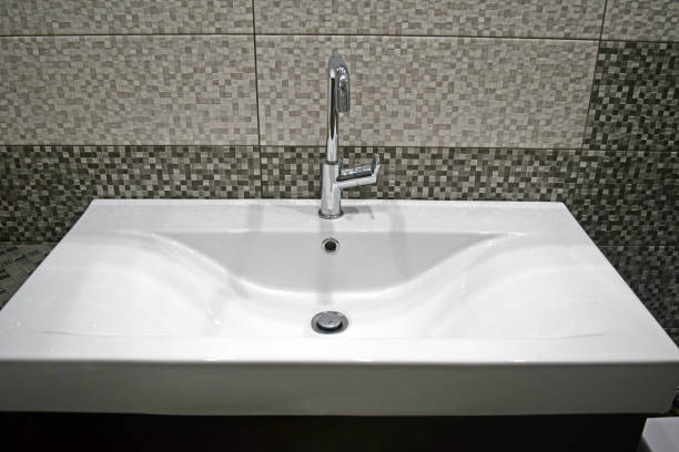 Detail of a rectangular white sink on gray mosaic tiles background.