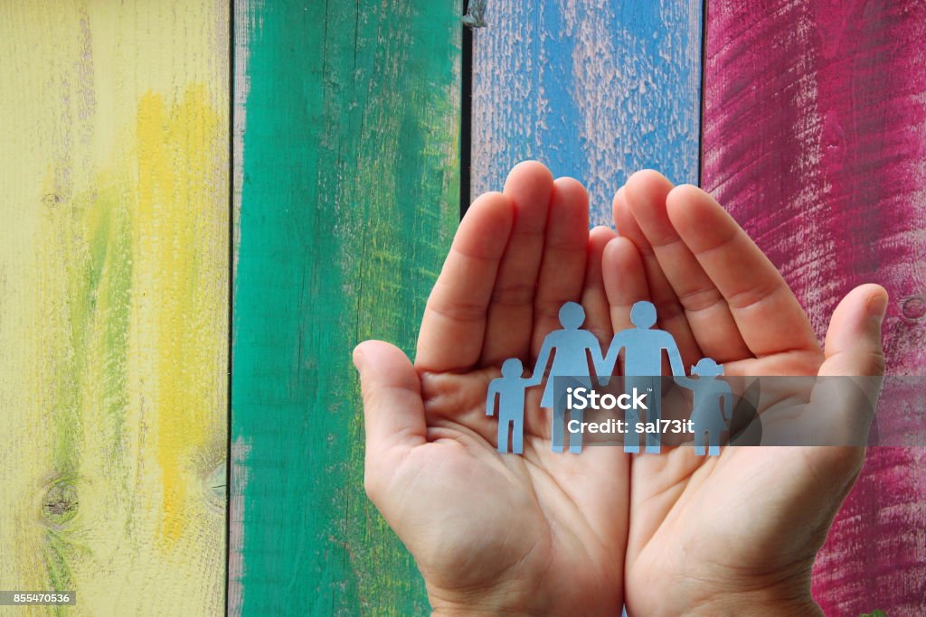 Famiglia di carta in mano su un concetto di benessere dello sfondo colorato in legno - Foto stock royalty-free di Protezione