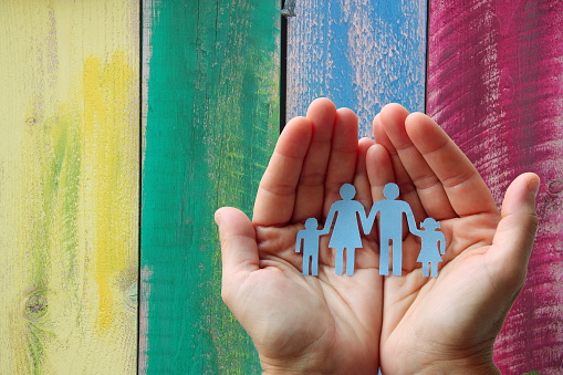 Paper family in hands on wooden coloured background welfare concept