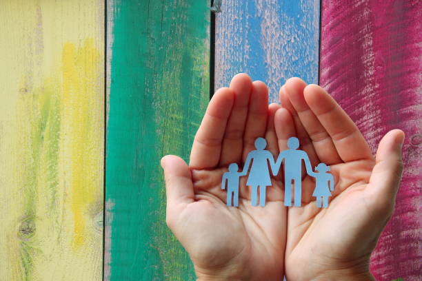Paper family in hands on wooden coloured background welfare concept Paper family in hands on wooden coloured background welfare concept social services stock pictures, royalty-free photos & images