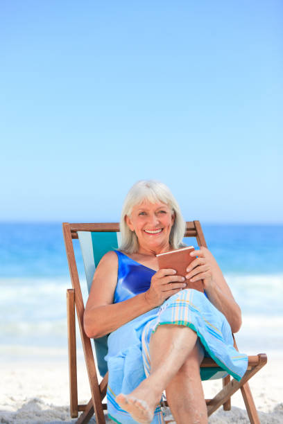 istock Senior woman reading a book on the beach 855471940