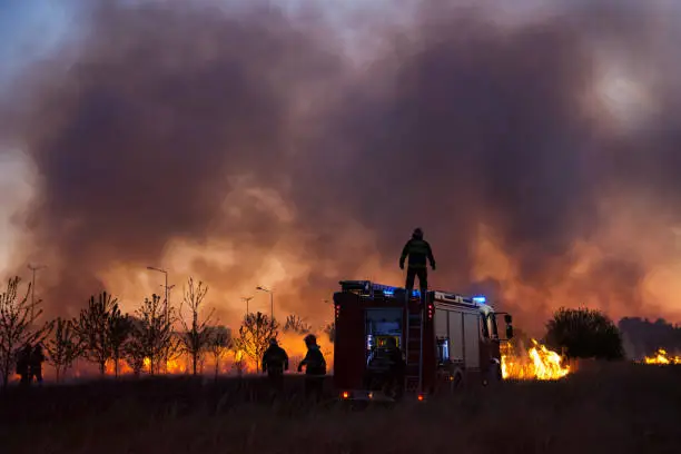 Photo of Fire truck and group of firefighters fighting bush fire in the evening.