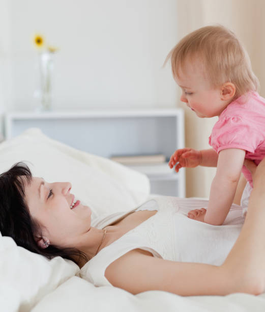 istock Lovely brunette woman playing with her baby while lying on a bed 855478220