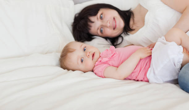 istock Beautiful brunette female posing with her baby while lying on a bed 855478540