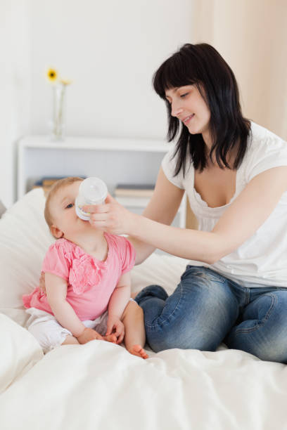 istock Pretty brunette female bottlefeeding her baby on a bed 855483942