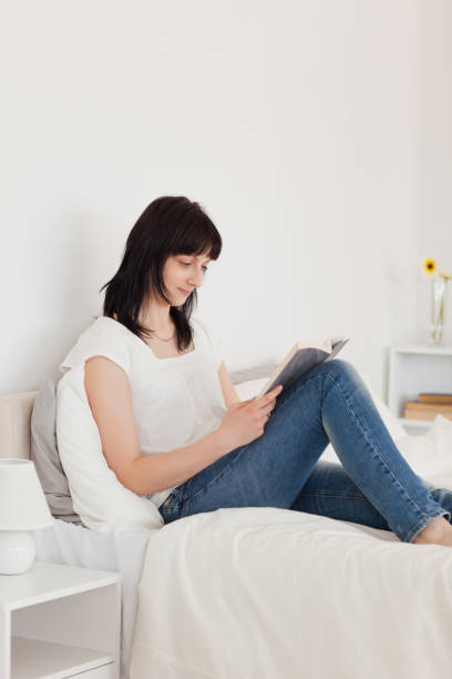 istock Charming brunette woman reading a book while sitting on a bed 855484342