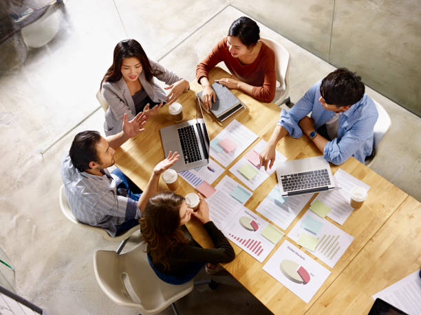 multiethnic business team meeting in office high angle view of a team of asian and caucasian corporate executives discussing business in meeting room. east asia stock pictures, royalty-free photos & images