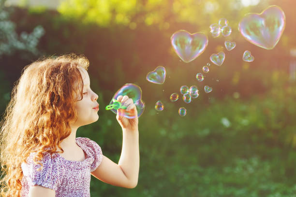 istock Curly girl blowing soap bubbles with heart shaped 855497902