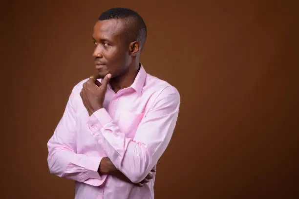 Photo of Studio shot of muscular African businessman wearing pink shirt against colored background