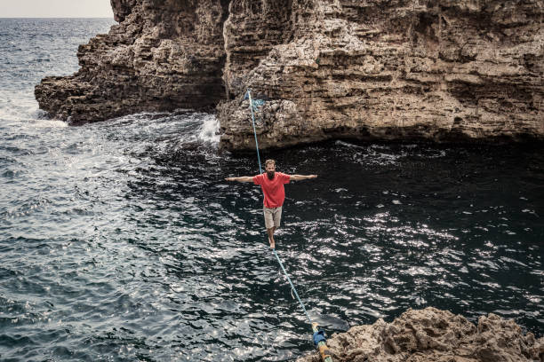 Man practicing slacklining over the sea Man practicing slackline highlining stock pictures, royalty-free photos & images