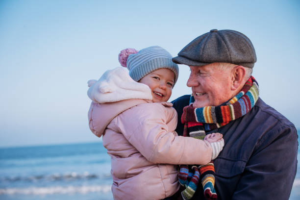 Grandfather with his Granddaughter on the Coast Senior man on the coast. Its cold outside so they are wrapped up warm. The man is carrying a little girl in his arms grandchild photos stock pictures, royalty-free photos & images