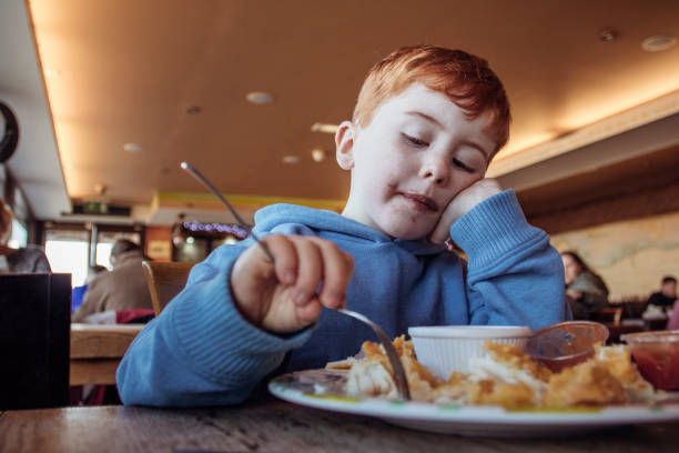 istock Little Boy Eating Fish and Chips in a Beach Cafe 855520798