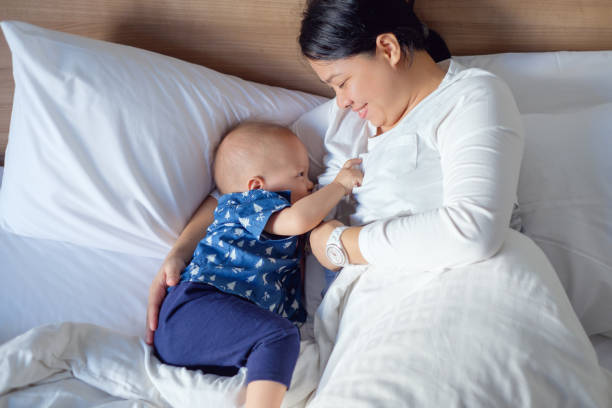 madre asiatica sta allattando carino piccolo asiatico 14 mesi / bambino bambino di 1 anno a letto - sucking asian ethnicity baby mother foto e immagini stock