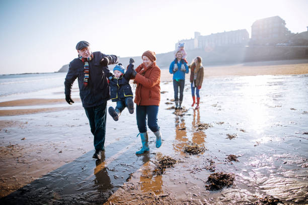 multi-generationen-familie am strand entlang spazieren - kälte fotos stock-fotos und bilder