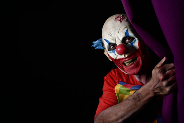 istock scary evil clown peering out from a stage curtain 855524334