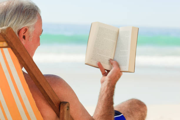 istock Senior man reading a book at the beach 855524856