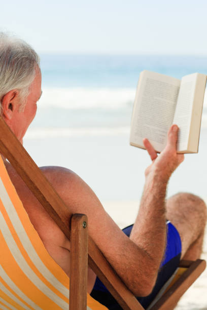 istock Senior man reading a book at the beach 855524882