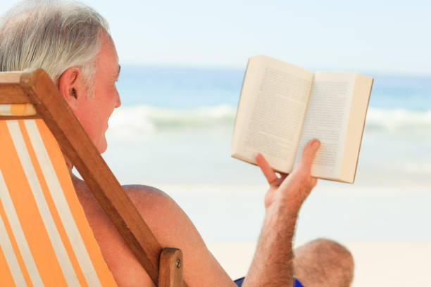 istock Senior man reading a book at the beach 855525030