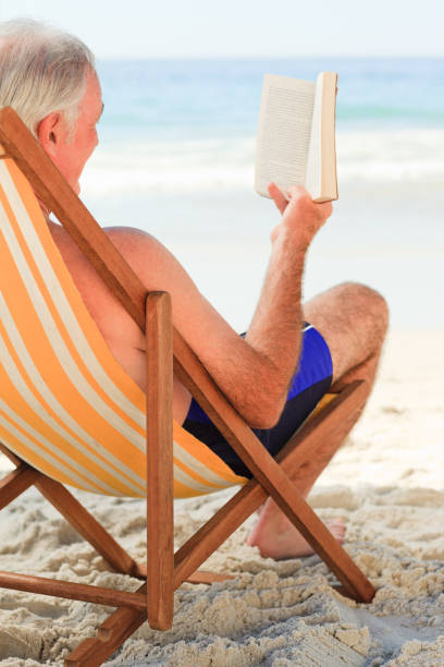 istock Senior man reading a book at the beach 855525064
