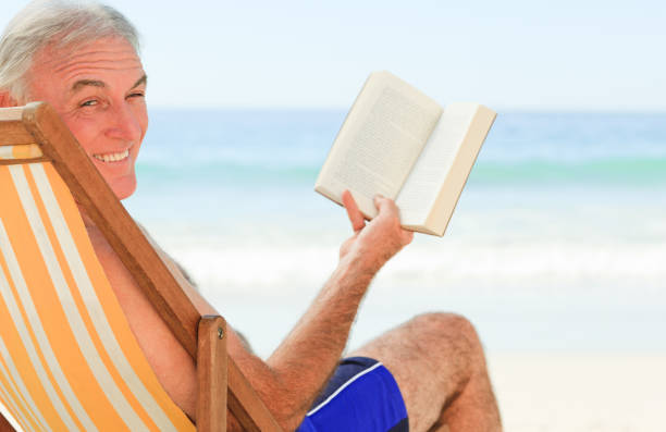 istock Senior man reading a book at the beach 855525072