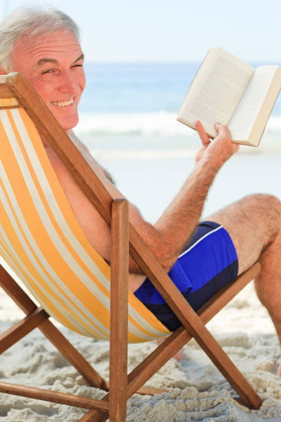istock Senior man reading a book at the beach 855525108
