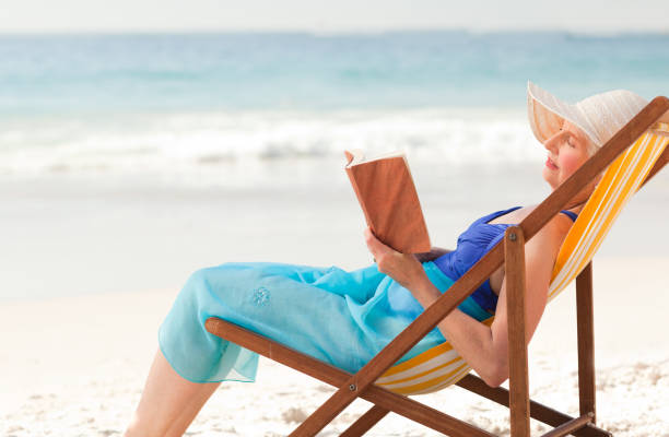 istock Elderly woman reading a book at the beach 855529158