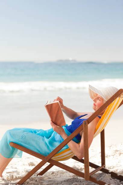 istock Elderly woman reading a book at the beach 855529190