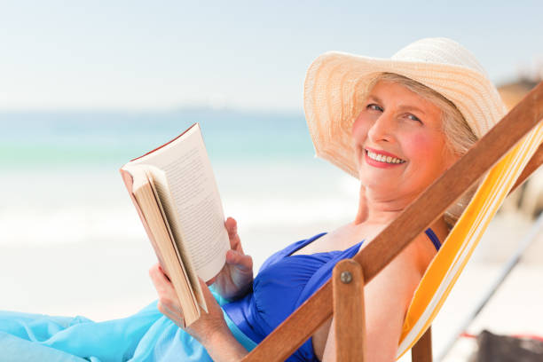 istock Elderly woman reading a book at the beach 855529250