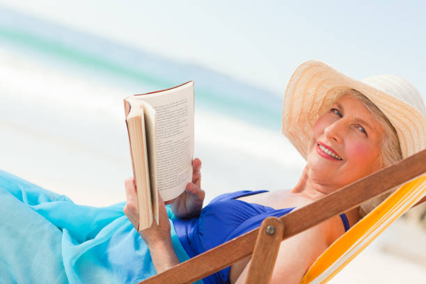 istock Elderly woman reading a book at the beach 855529282