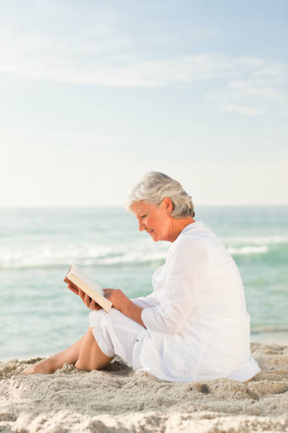 istock Elderly woman reading her book on the beach 855581662