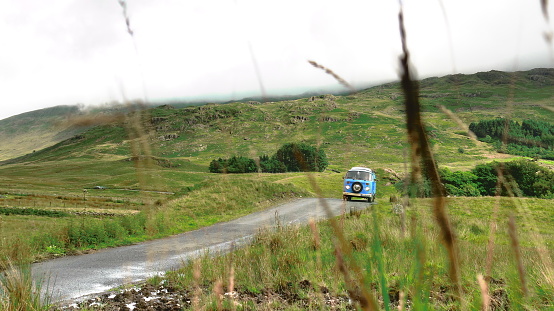 Lake District National Park, Windermere, England - July, 26th, 2017:A blue classic VW Bus from 1973 driving westbound while the clouds are rolling in on Hawkshead passroad, one of the highest passroads in Great Britain.