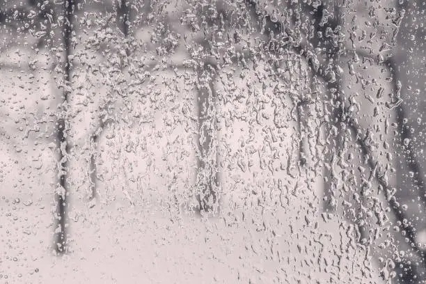 Texture of the ice and drops on the window glass in a bad winter day, close up. Photo black and white, toned