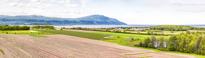 Panorama, panoramic aerial view of farmland in Ile D'Orleans, Quebec, Canada, plowed field, furrows, land, farm, house, barn, shed, Saint Lawrence river, hills, mountains and distant village