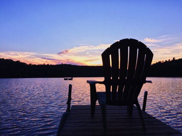 Silhouette of an adirondack chair against the sun setting and reflecting on the lake stock photo