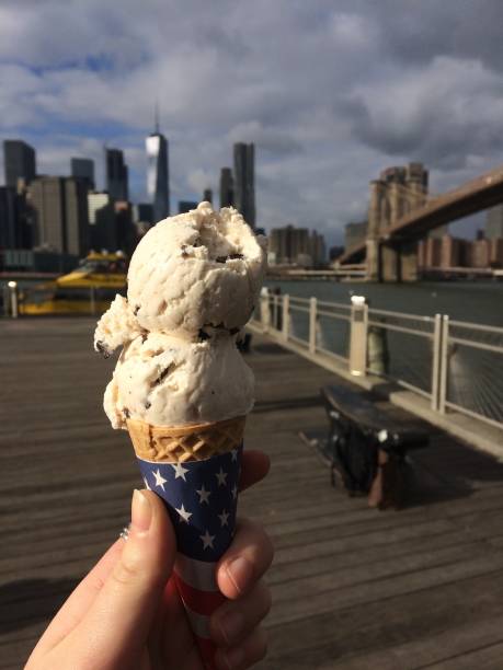 Hand holds a double scoop ice cream cone with an american flag against the New York Skyline stock photo
