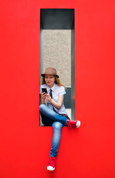 Beautiful girl texting on smartphone. Red background. Modern life.