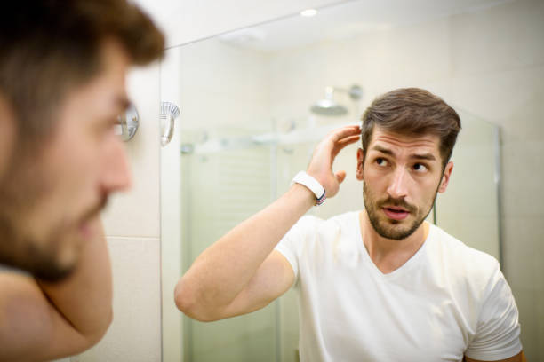 Man in the bathroom Young man in the bathroom looking in the mirror and fixing his hair. dandruff men stock pictures, royalty-free photos & images