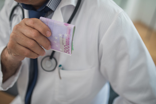 Doctor putting bribe money in pocket, in his office, cropped photo.