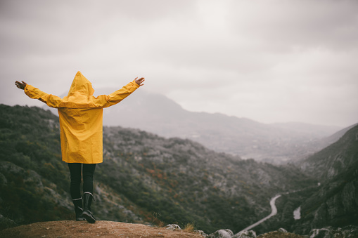 Young woman in the yellow raincoat standing on the top of the mountain