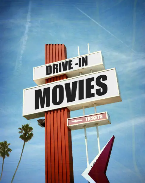 aged and worn vintage photo of drive in movies sign with palm trees
