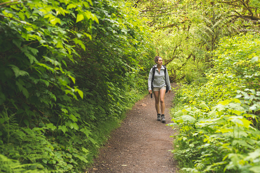 Young ethnic woman hikes on trail through a lush forest. She is alone and has a backpack on.