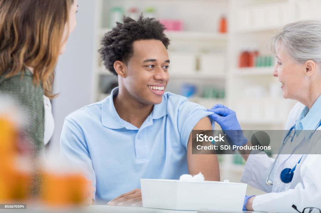 Giovane sorride in sollievo al farmacista dopo vaccinazione antinfluenzale - Foto stock royalty-free di Vaccino