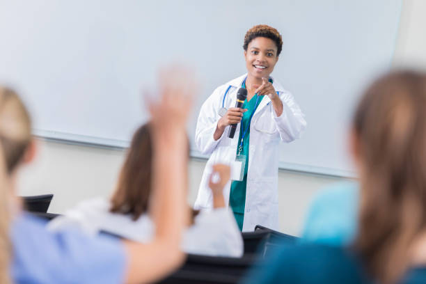 Female doctor teaches a class at medical school Confident African American female doctor points to a student taking a class at a medical school. An unrecognizable female student has her arm raised. The doctor is pointing to that person. medical education stock pictures, royalty-free photos & images